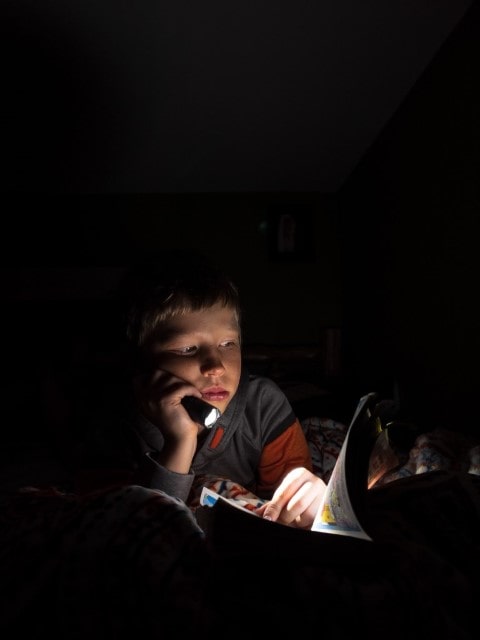 child reading at night with a flashlight