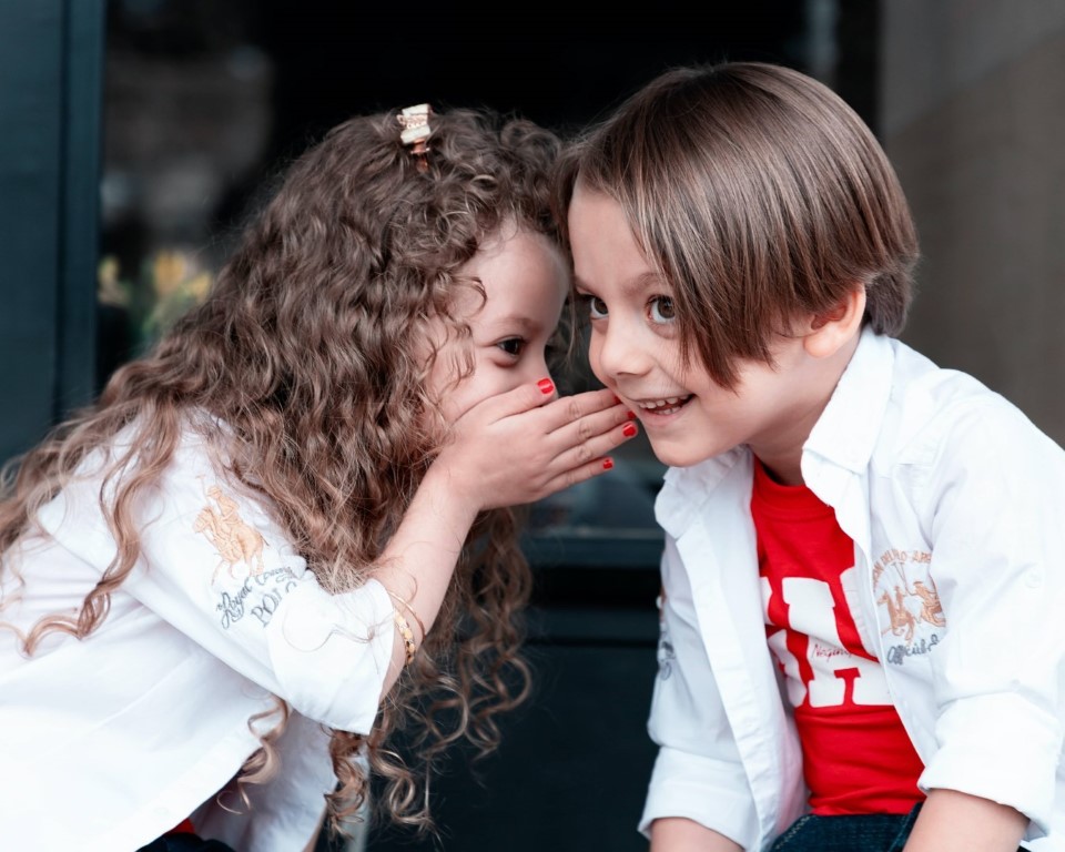 big image of two smiling children whispering to each other